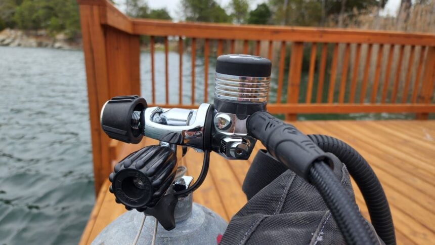 Aqualung Leg3nd Elite first stage clamped to a tank valve on the dock, water and railing behind
