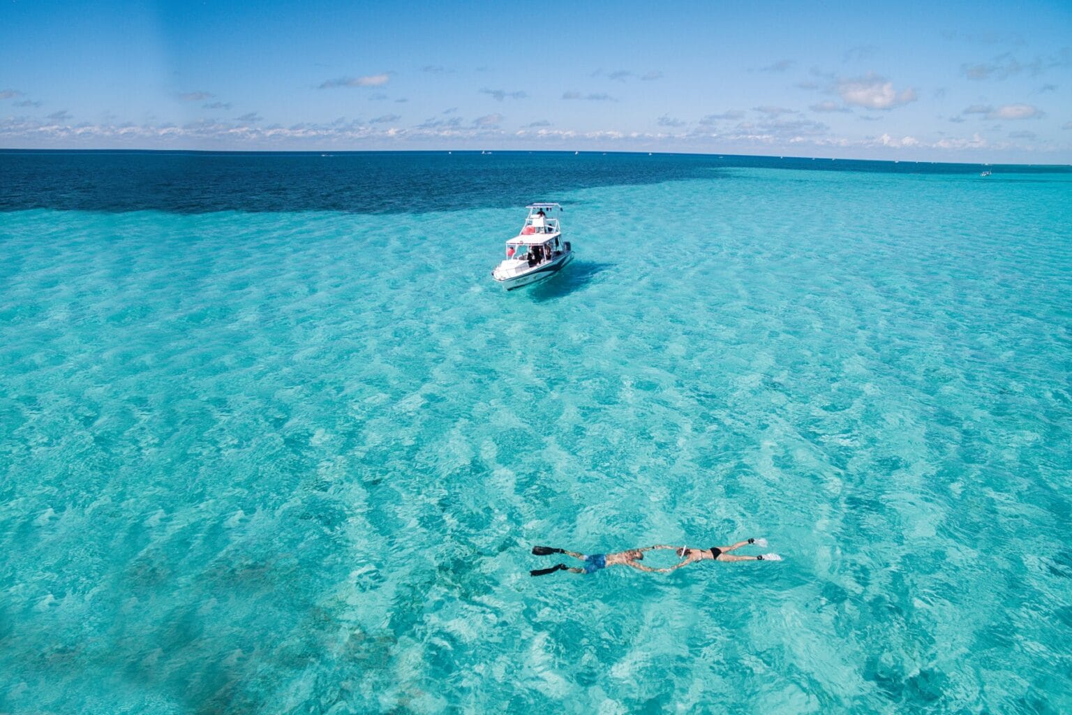 Two snorkelers floating in shallow turquoise water with a dive boat anchored nearby