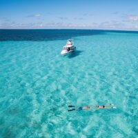 Two snorkelers floating in shallow turquoise water with a dive boat anchored nearby