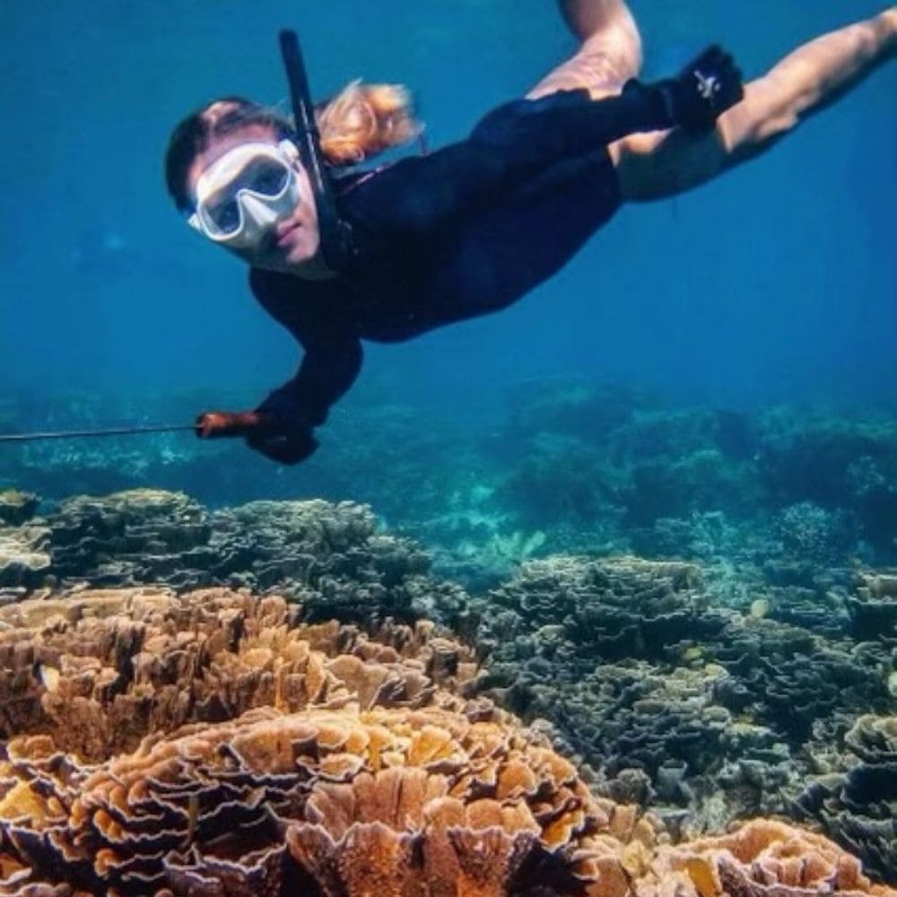 freediver in a wetsuit gliding over a coral reef