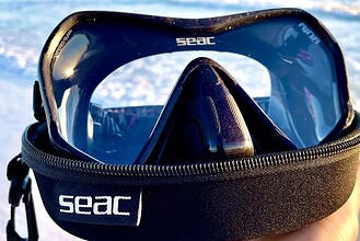 SEAC Ajna mask with a dark tinted lens resting on its branded zip case in front of the surf