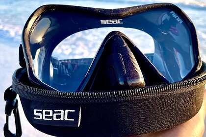 SEAC Ajna mask with a dark tinted lens resting on its branded zip case in front of the surf
