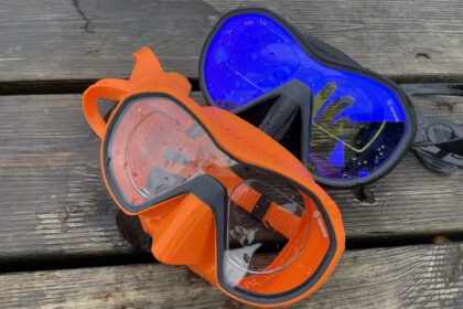Two Apeks VX1 masks in orange and blue sitting wet on a pier after a DIVEIN test dive