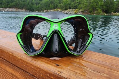 Mares X-Vision mask in green and black resting on a wet wooden railing above a lake