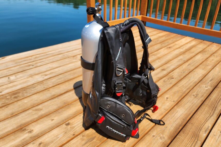 Atomic Aquatics BC2 BCD rigged to a scuba tank, standing on a wooden dock beside a quarry lake