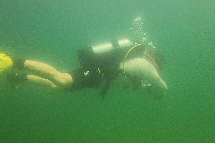 DIVEIN tester finning through murky green freshwater in the Oceanic Biolite BCD