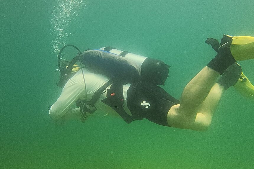 DIVEIN tester finning through green water with the Dive Rite Hydro Lite wing inflated behind