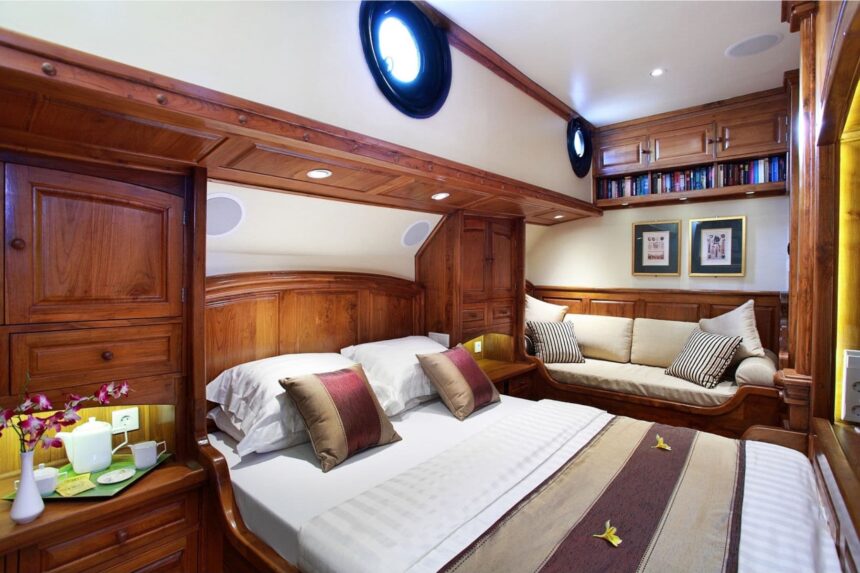 wood paneled cabin aboard the Adelaar with a double bed and bookshelf