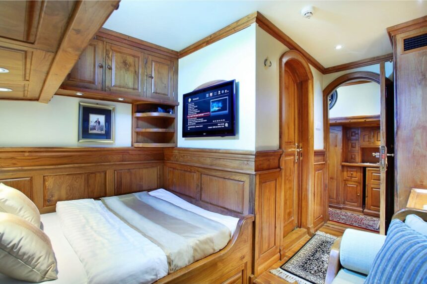 wood paneled cabin aboard the Adelaar with a bed and wall mounted TV