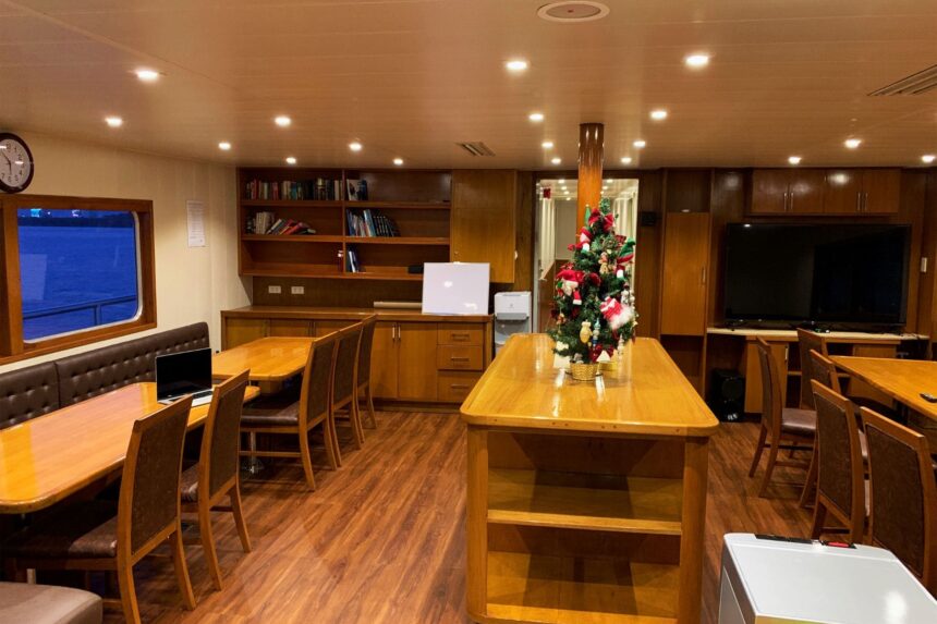 wood paneled lounge aboard the Infiniti with dining tables and a small Christmas tree