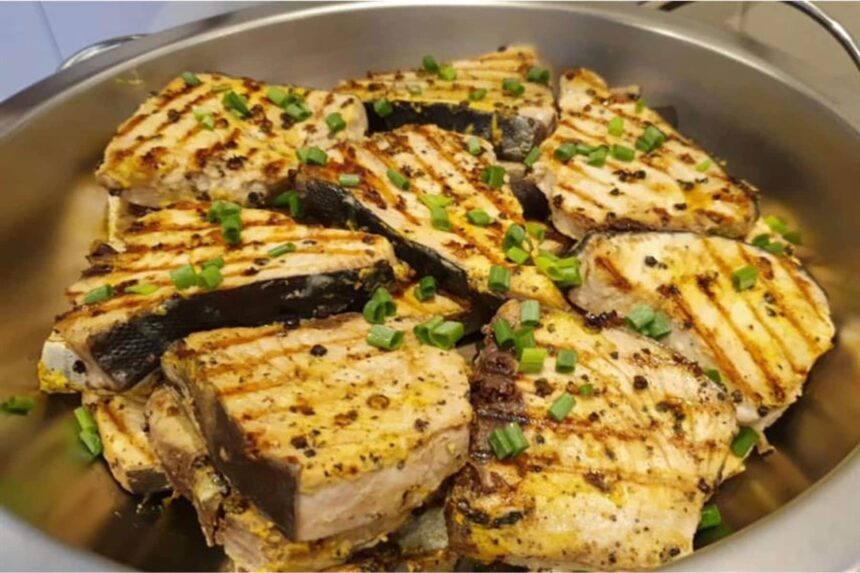 grilled fish steaks topped with chopped scallions in a serving pan