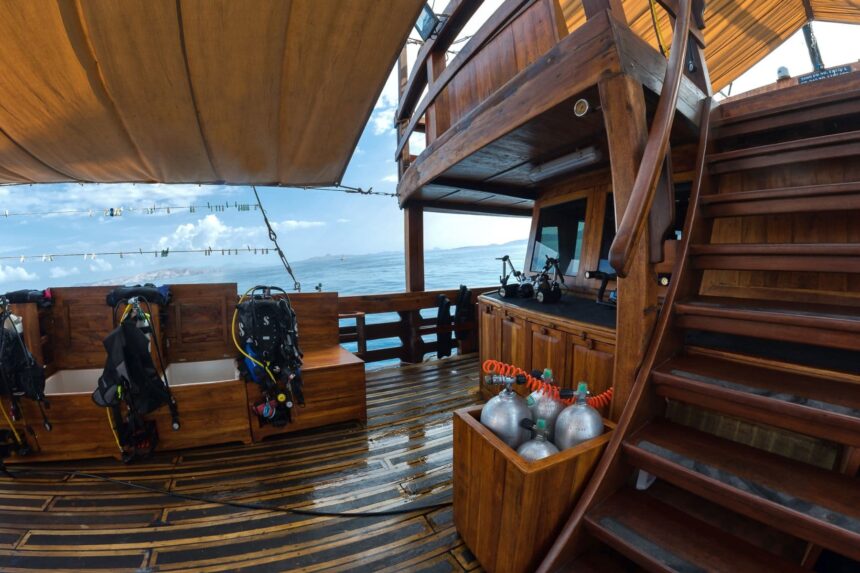 Dive deck of the Damai I liveaboard with scuba gear and tanks staged under a canvas awning