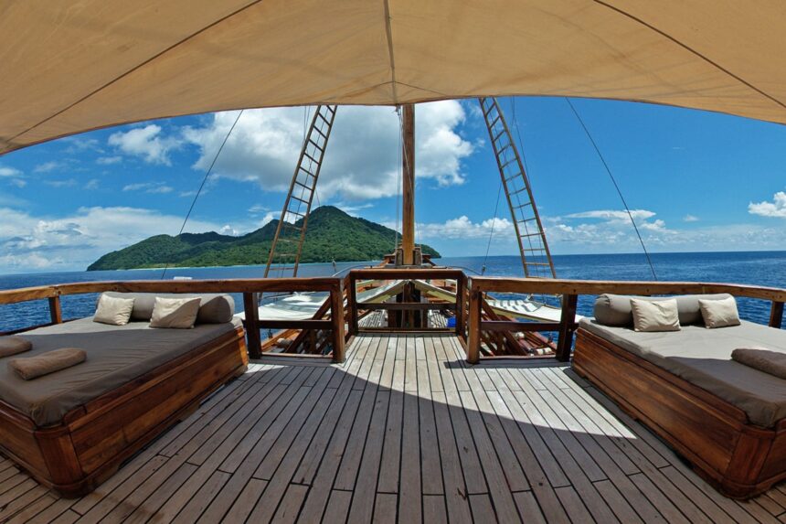 Shaded daybeds on the Damai II's foredeck overlooking a forested island and open sea