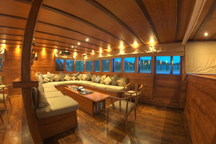 Wood-paneled salon aboard the Damai II liveaboard with wraparound seating and evening lighting