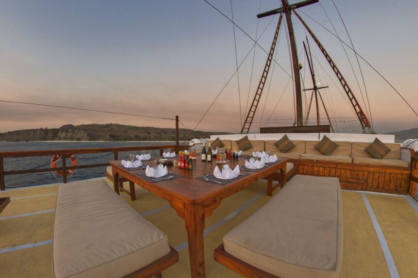 Outdoor dining table set for dinner on the Damai II's deck at dusk with a coastal backdrop