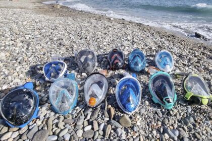 Rows of full face snorkel masks lined up on a pebble beach beside the surf