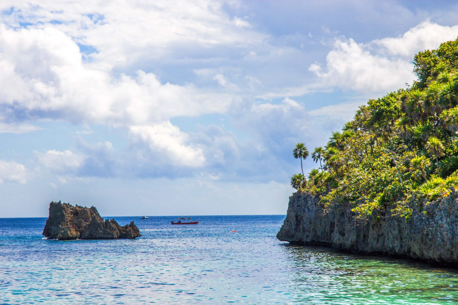 Limestone cliff and sea stack on the Roatan coast with a small boat on flat blue water