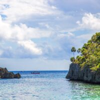 Limestone cliff and sea stack on the Roatan coast with a small boat on flat blue water