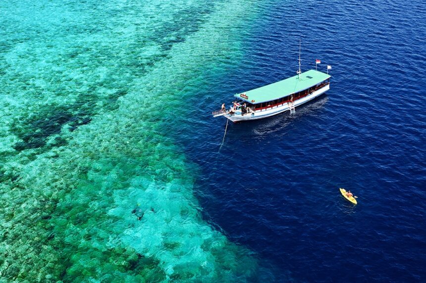 dive boat anchored at the edge of a coral reef with a kayaker nearby