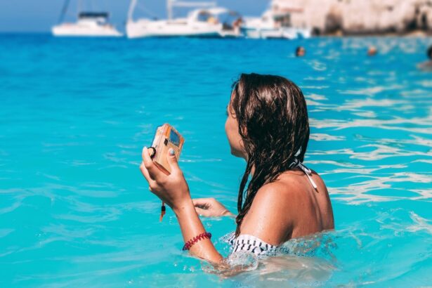 Woman standing chest-deep in turquoise sea holding a compact waterproof camera, boats anchored behind her