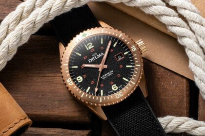 Delma Cayman automatic dive watch with a bronze case and black dial resting on wood beside rope