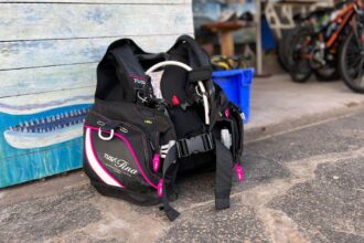 TUSA Tina BCD in black with pink trim standing on the ground outside a dive shop
