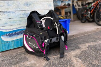 TUSA Tina BCD in black with pink trim standing on the ground outside a dive shop