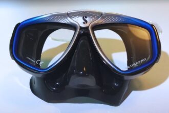 ScubaPro Zoom dive mask with a black skirt and blue framed twin lenses standing on a white surface