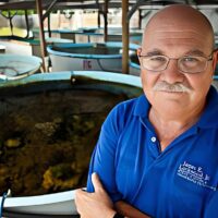 Dr. Alex Brylske standing in front of large aquaculture tanks in a blue polo shirt