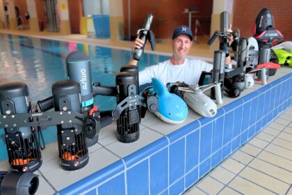 DIVEIN tester behind a poolside lineup of underwater scooters lined up for side by side testing