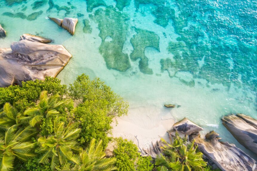 Aerial view of a white sand cove ringed by granite boulders and palm trees on a Seychelles island