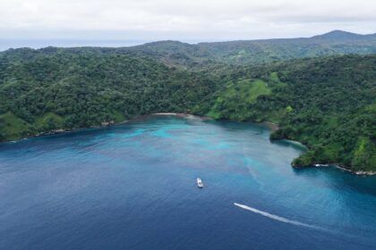 Aerial view of Chatham Bay at Cocos Island with a boat anchored over turquoise reef below forested hills