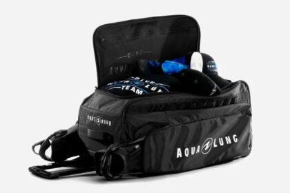 Black Aqua Lung wheeled dive duffel opened up with kit packed inside on a plain background