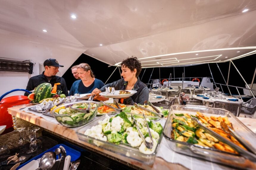 Crew and guests plating food from a buffet spread of salads and grilled vegetables aboard the Humboldt Explorer