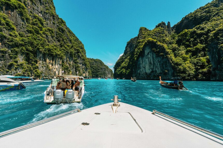 Boat bow approaching a turquoise lagoon lined with steep limestone cliffs and other tour boats nearby
