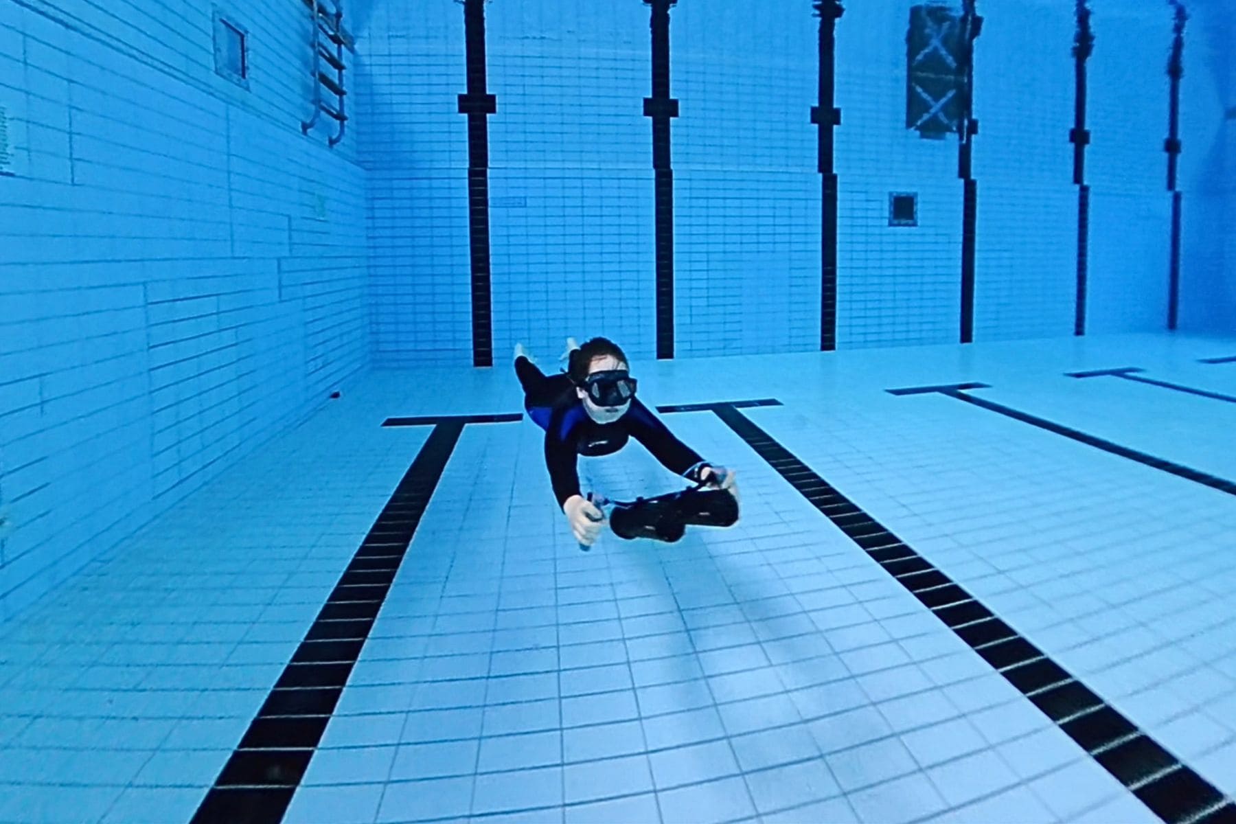 Young DIVEIN tester gliding across the bottom of a deep tiled pool on a timed Finmos scooter speed run