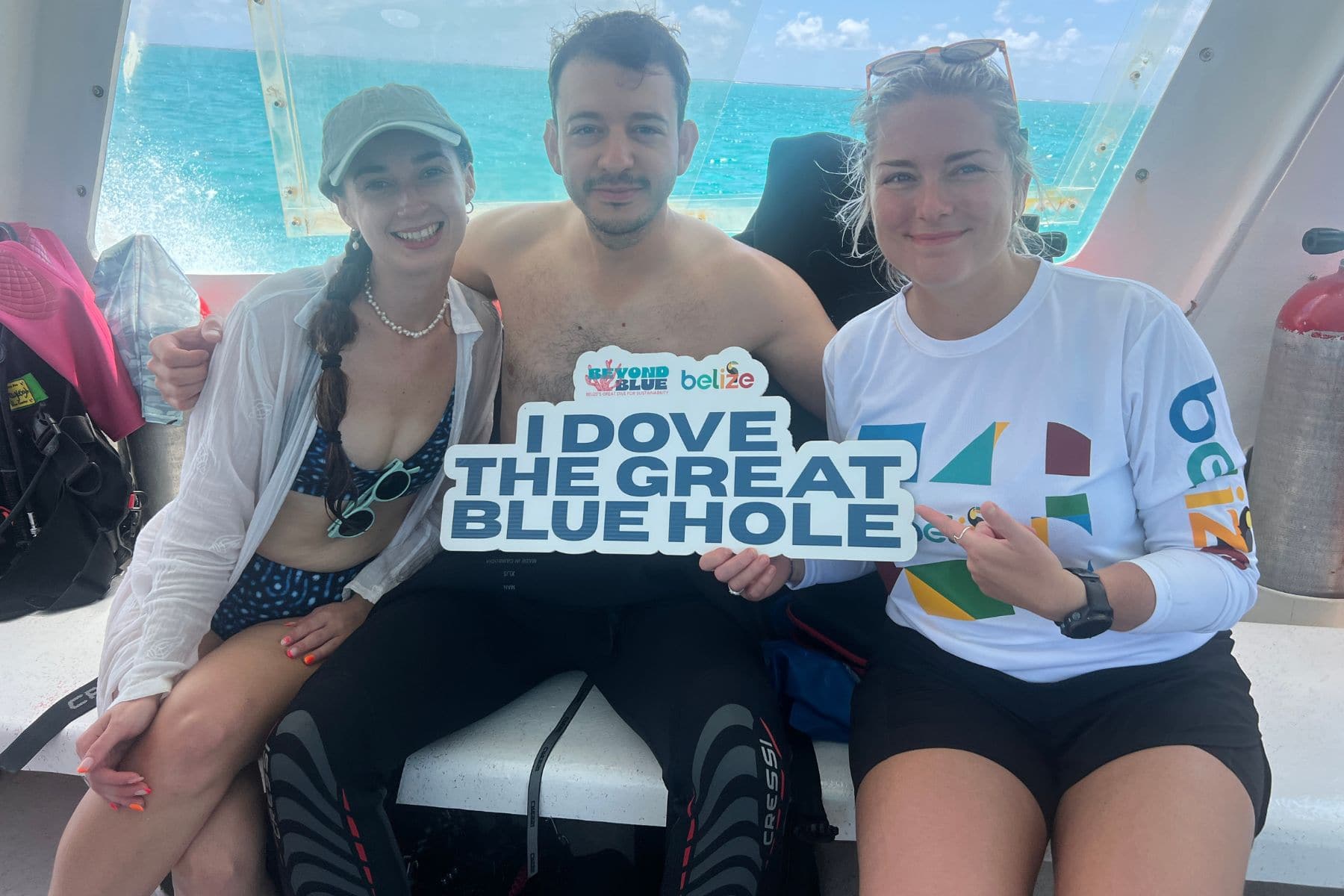 Three divers on a boat holding a sign reading I Dove The Great Blue Hole in Belize