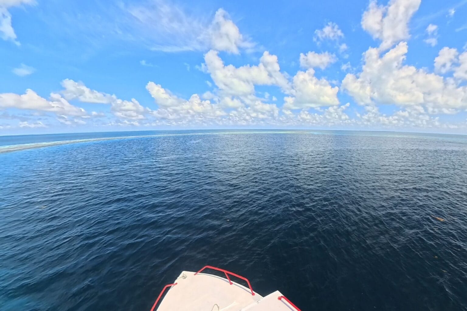 Boat bow heading out across open ocean toward the Belize Barrier Reef under a partly cloudy sky