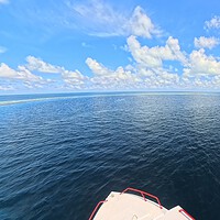 Boat bow heading out across open ocean toward the Belize Barrier Reef under a partly cloudy sky