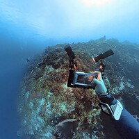 DIVEIN tester holding a DiveVolk phone housing rigged with two video lights over a reef
