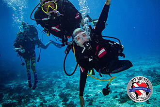 An amputee adaptive diver underwater alongside a Diveheart dive buddy
