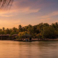 Over-water bungalows and a thatched dock hut at Anthony's Key Resort on Roatan, lit by an orange sunset over calm water