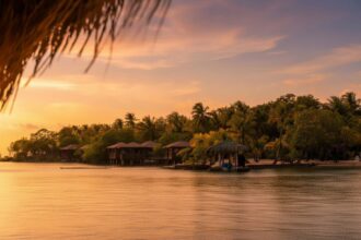 Over-water bungalows and a thatched dock hut at Anthony's Key Resort on Roatan, lit by an orange sunset over calm water