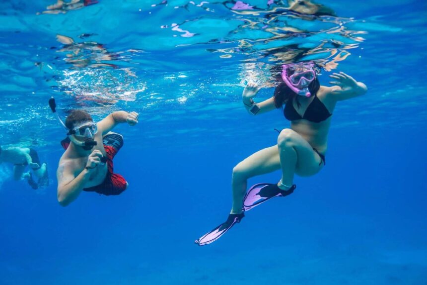 Two snorkelers at the surface in clear blue water, one wearing a pink Promate mask, snorkel and fins